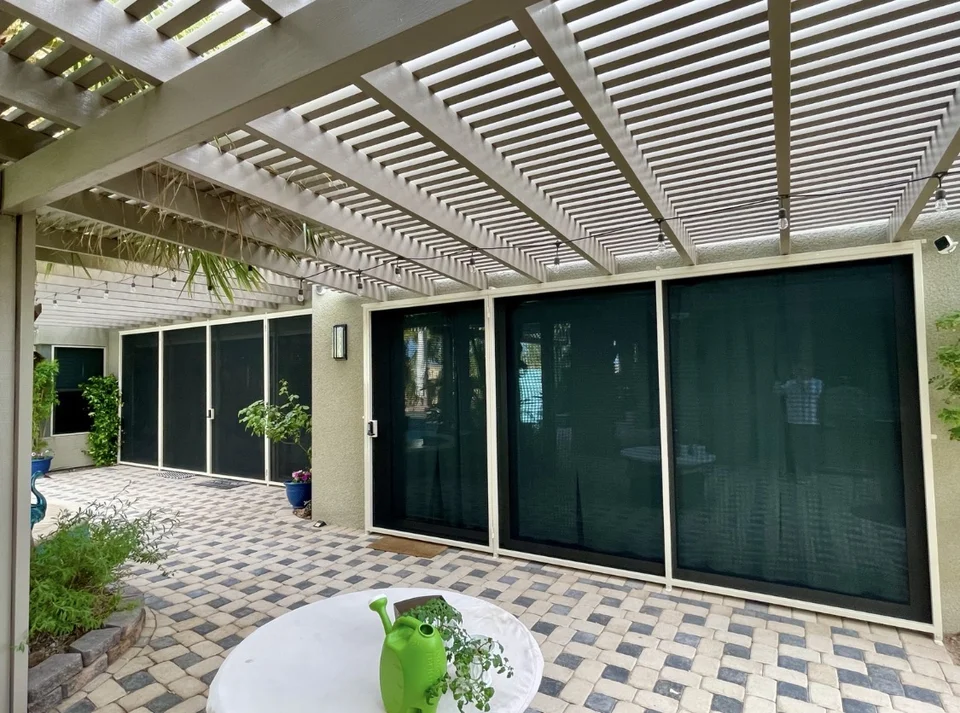 Olson Iron security screen patio sliders with dark mesh, white frame, pergola overhead, and lush patio landscaping — Las Vegas