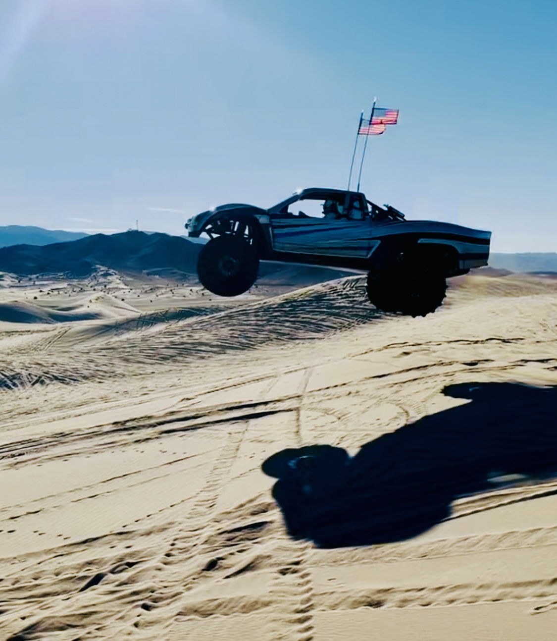 Off-road vehicle airborne over sand dunes with American flag