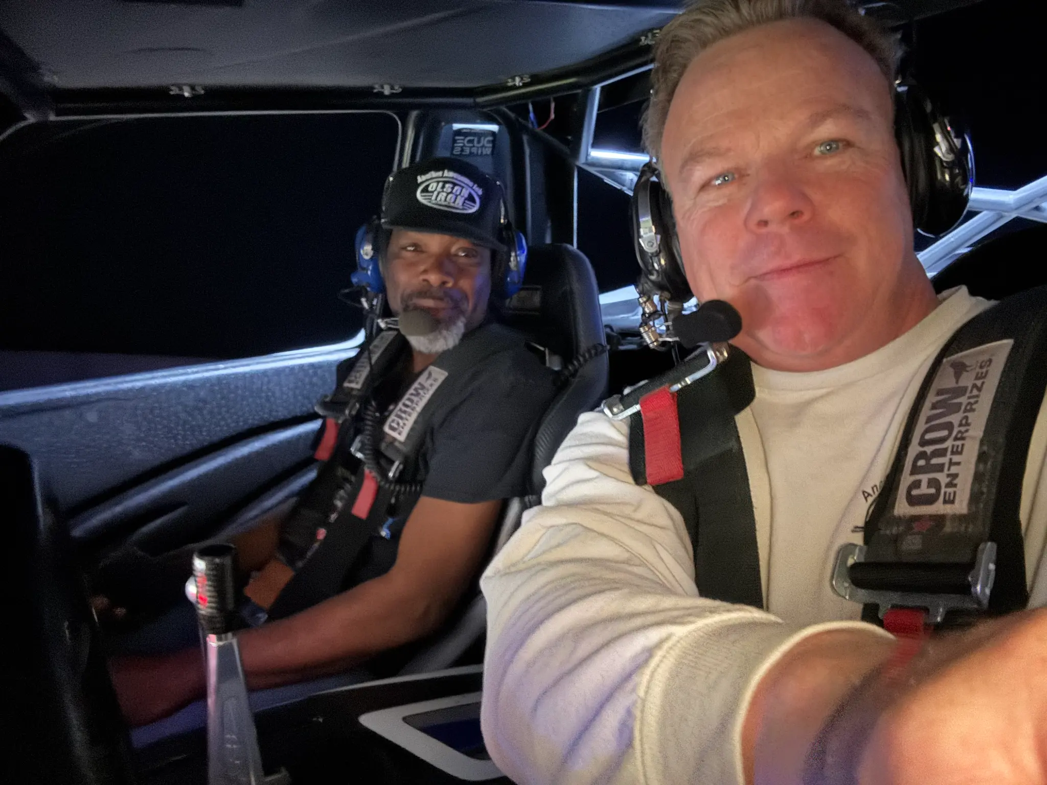 Two crew members inside an off-road vehicle at night with harnesses