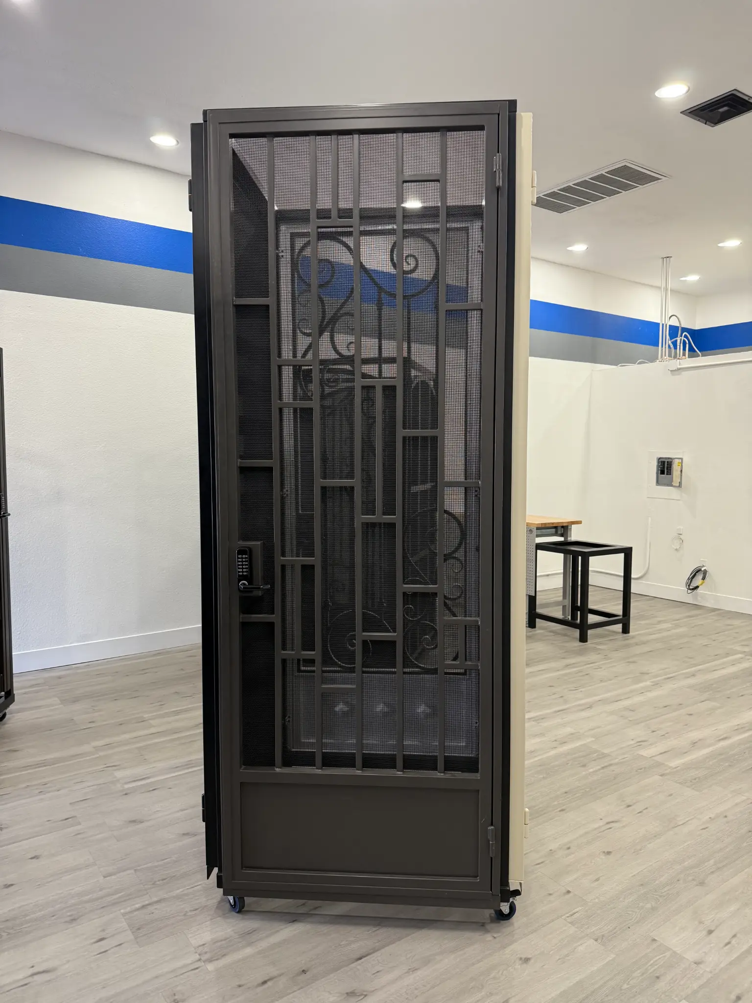 Dark gray security screen door with scrollwork and keypad lock in Olson Iron showroom