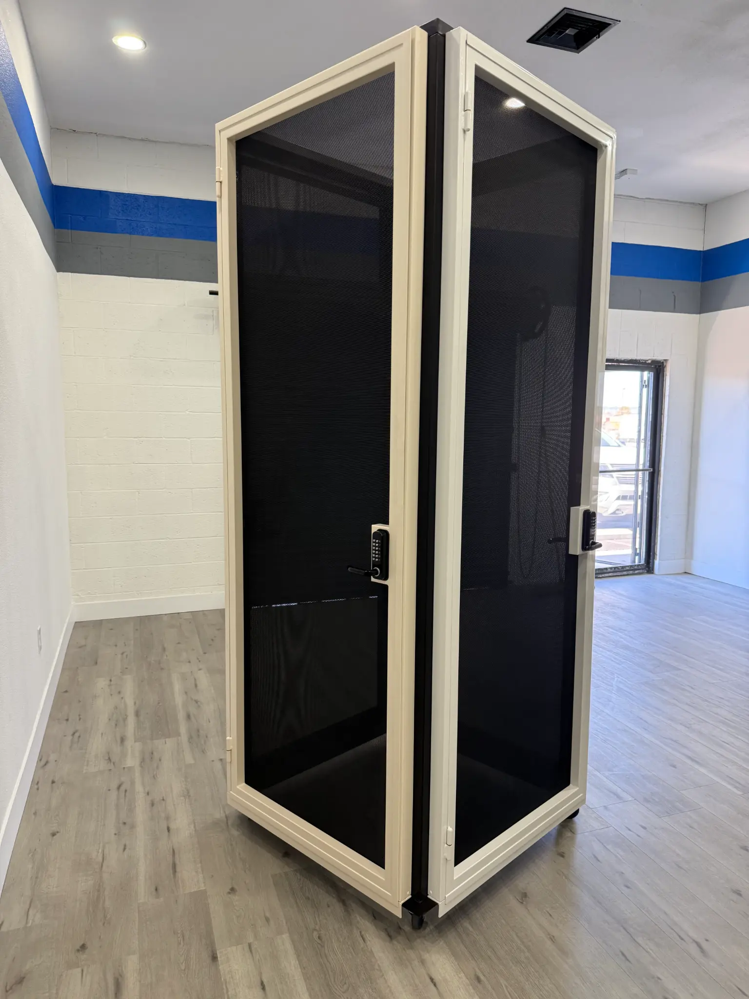 White-framed security enclosure with black mesh and keypad in Olson Iron showroom