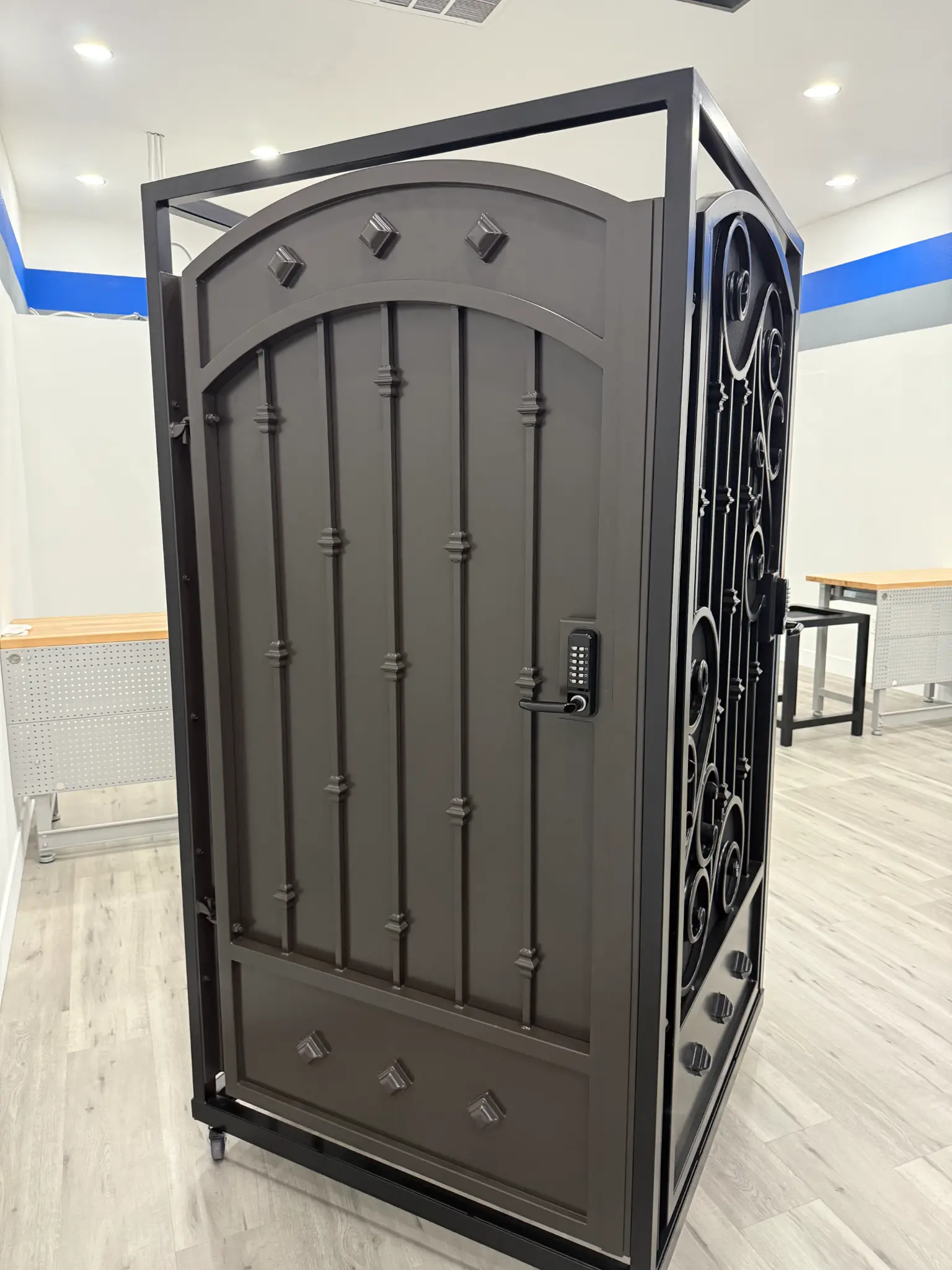Bronze-colored metal gate with arched top and keypad in Olson Iron showroom