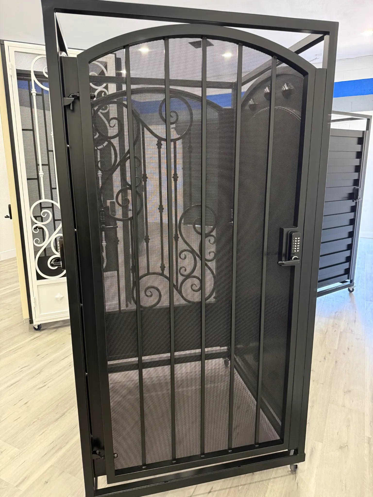 Black security screen door with scrollwork and keypad in Olson Iron showroom