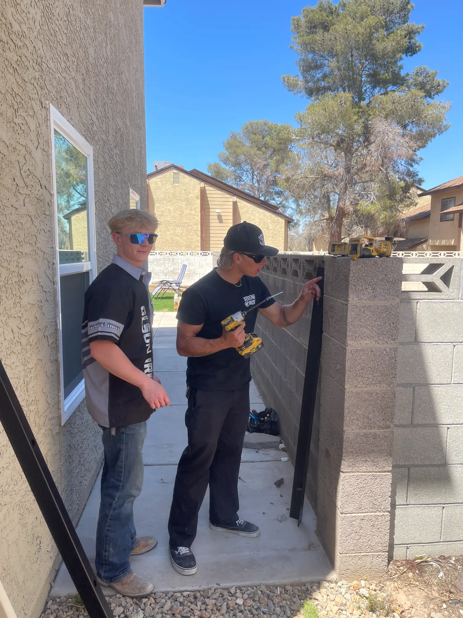 Landon and Jay drilling a gate post together on a job site